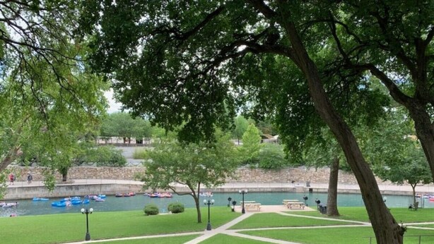 Ein Park mit einem Gehweg, Bänken und einem Fluss mit Booten.