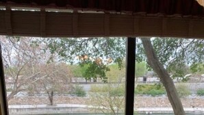 Ein Essbereich mit Tisch und Stühlen, Blick auf einen Park mit Weg und Bäumen, und ein Gebäude im Hintergrund.