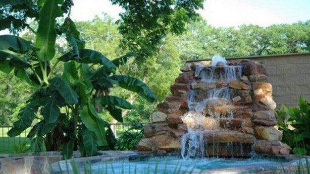 A stone waterfall feature with a pool at the base, surrounded by lush greenery.