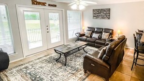 A living room with a sofa set, a coffee table, and a ceiling fan. There are two doors with a view of the outside.