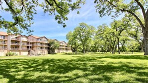 A multi-story building with balconies, surrounded by a grassy park area with trees and picnic tables.