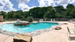A swimming pool with a stone edge, surrounded by a stone deck and a metal fence.