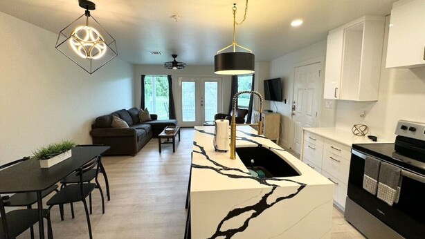 A modern kitchen with a marble island, black and white cabinets, and a dining area with a black table and chairs. - Hill Country Hideout | Sleeps 10 | WiFi | 2 Patios (New Braunfels)