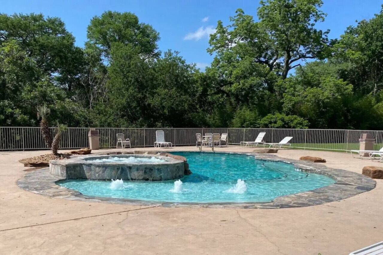 A circular hot tub with a fountain in the center, surrounded by lounge chairs and a stone border.
