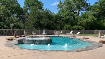 A circular hot tub with a fountain in the center, surrounded by lounge chairs and a stone border.