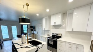 A modern kitchen with white cabinetry, a central island with a black and white marble design, a black stove, and a pendant light. - Hill Country Hideout | Sleeps 10 | WiFi | 2 Patios (New Braunfels)