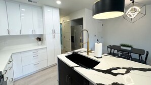 A modern kitchen with white cabinets, a black and white marble island, a gold faucet, and a pendant light. - Hill Country Hideout | Sleeps 10 | WiFi | 2 Patios (New Braunfels)