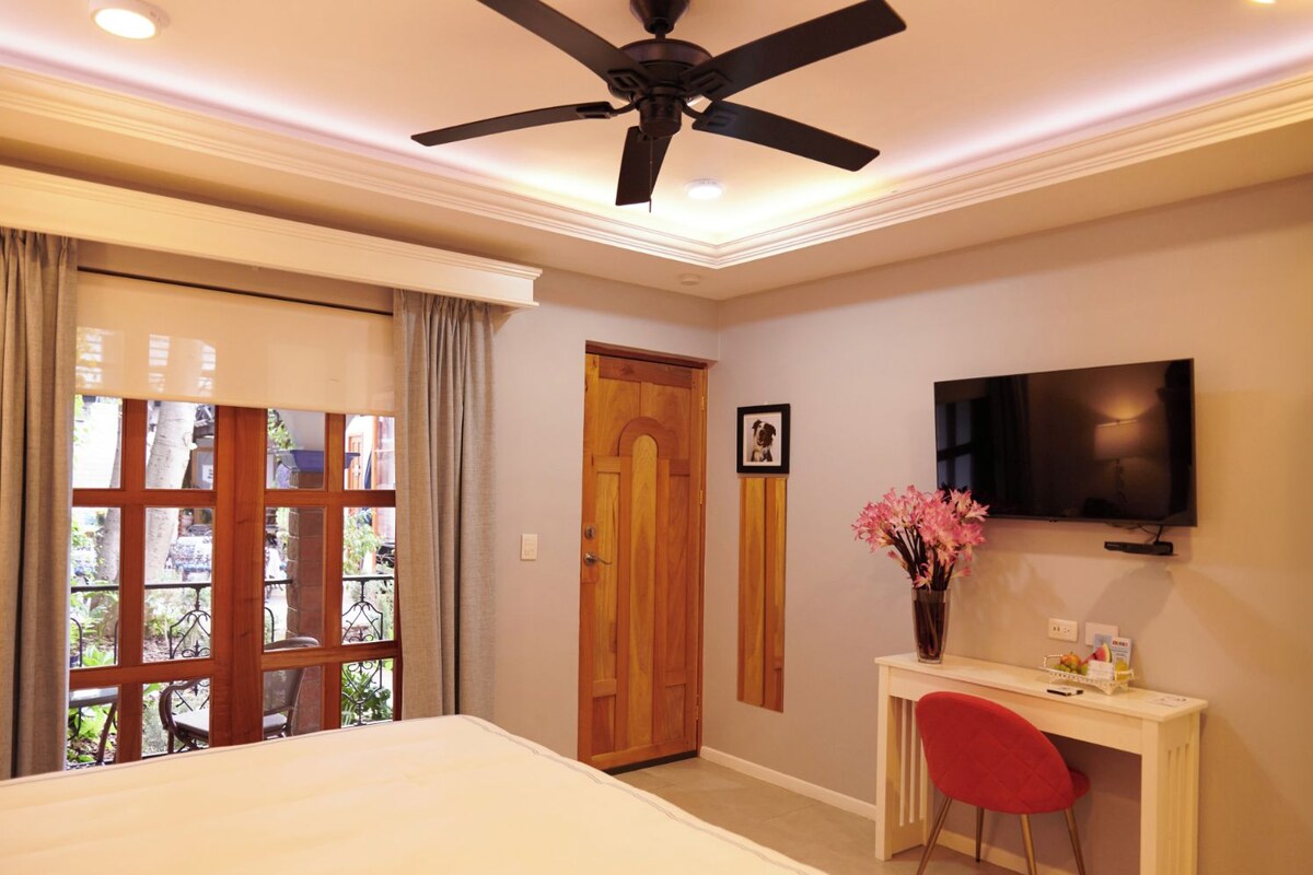 Una habitación de hotel con una cama, un escritorio con una silla roja, un televisor y una ventana con cortinas.