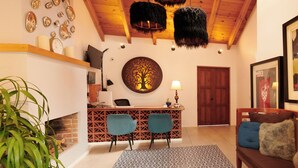 Une pièce chaleureuse avec un plafond en bois, un comptoir d’accueil avec deux chaises, un tapis à motifs et un canapé avec des coussins.