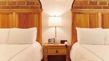 Une chambre avec deux lits, une table de chevet avec une lampe et un mur en briques.