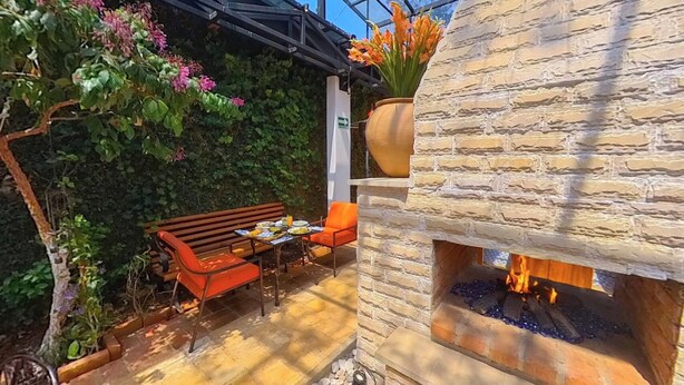 Un patio con una chimenea de piedra, asientos exteriores y un cerramiento de vidrio.