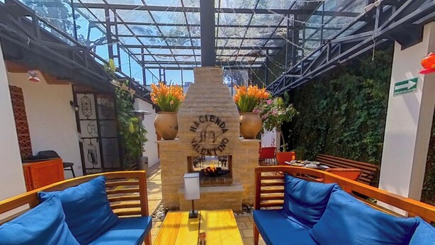 Un espace extérieur aménagé, abrité et doté de canapés bleus confortables, d’une cheminée en pierre au centre et de plantes en pot.
