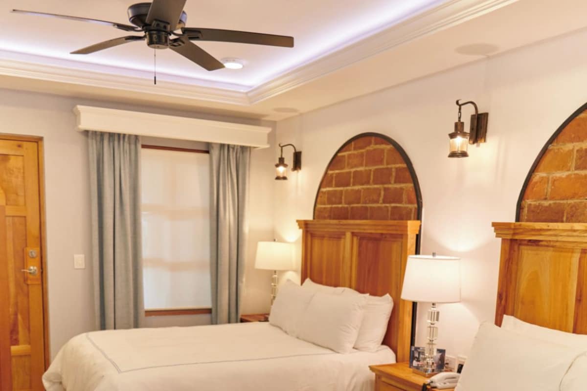 Habitación de hotel con dos camas, ventilador de techo y chimenea de ladrillo.