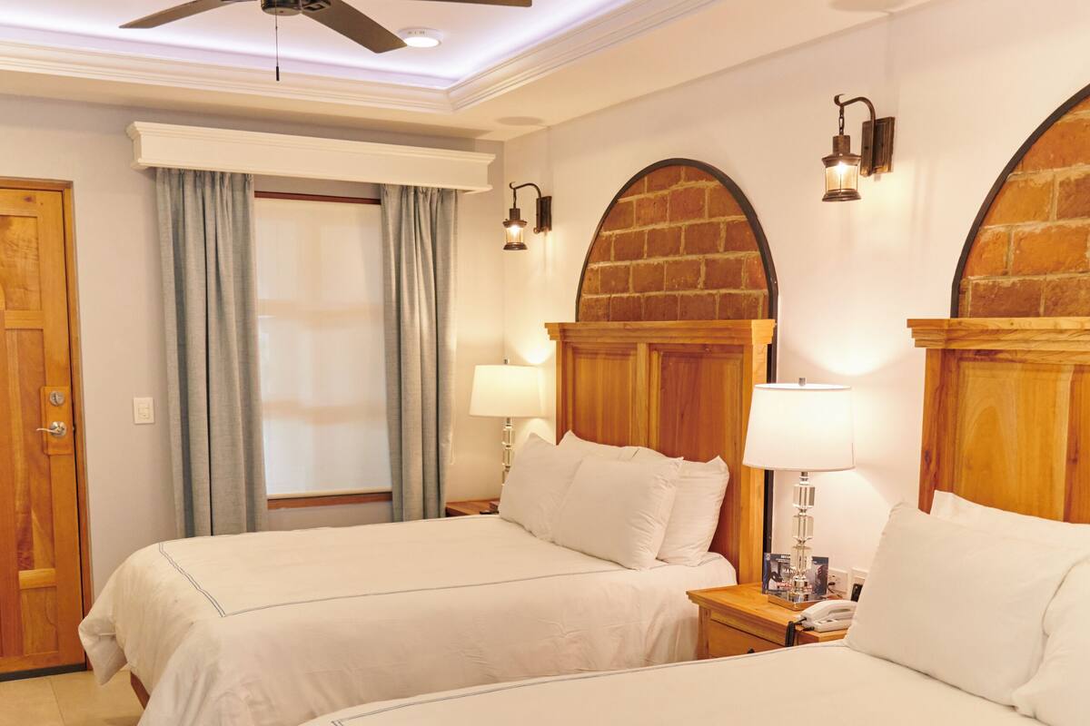 A hotel room with two beds, a ceiling fan, a wooden door, and a window with curtains.