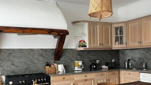 Een keuken met houten kasten, een zwart fornuis, een houten eettafel en een geweven lamp.