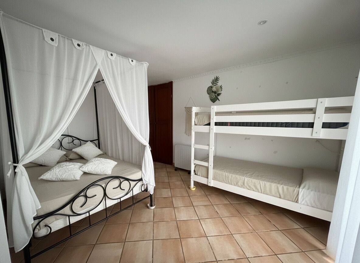 Une chambre avec un lit à baldaquin, un lit superposé, un sol carrelé et un élément décoratif mural.