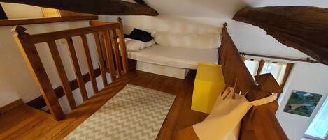 A loft bedroom with a wooden staircase, a white sofa, a patterned rug, and a painting on the wall.