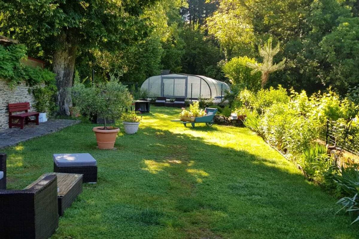 Un jardin avec une maison en pierre, une serre et du mobilier d’extérieur.