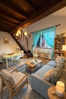 Uma sala de estar acolhedora com sofá, cadeiras, mesa de centro, estante de livros, escada e janela com cortinas.