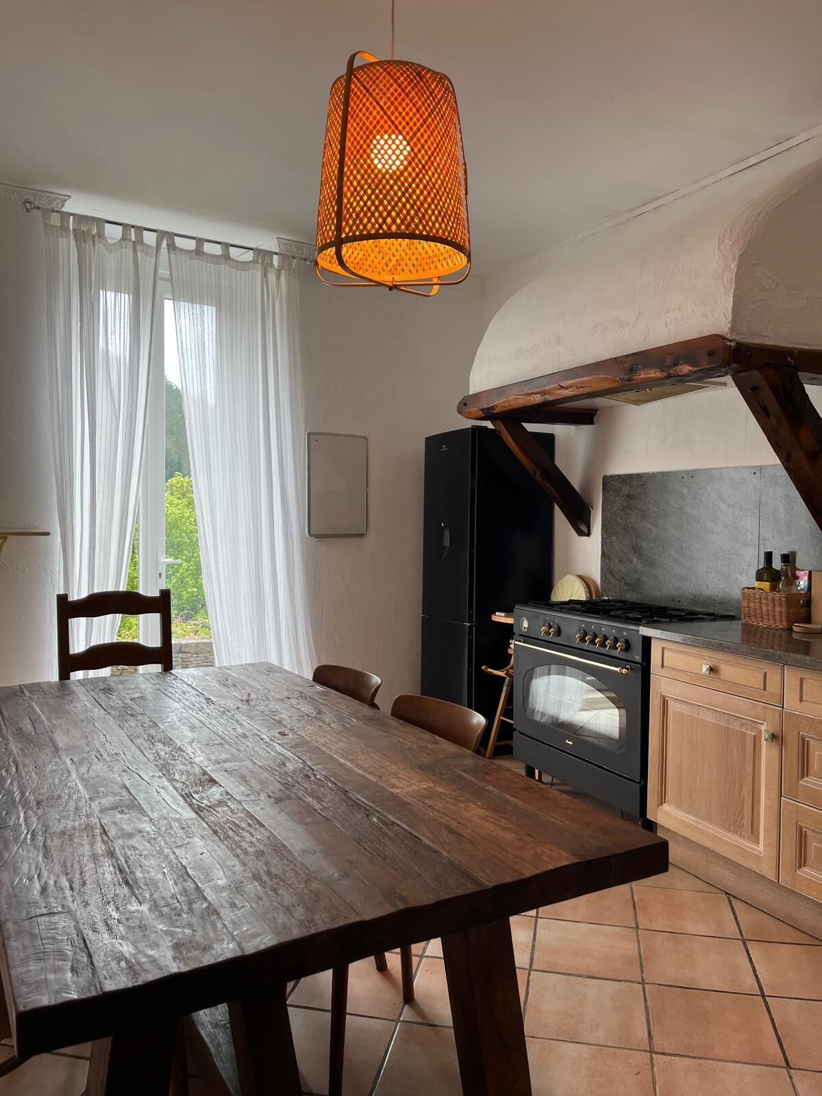 Una cocina rústica con una mesa de madera, una lámpara colgante naranja y vistas al verdor exterior.