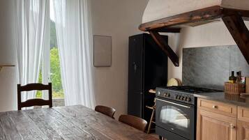 Una cocina rústica con una mesa de madera, una lámpara colgante naranja y vistas al verdor exterior.