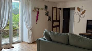 Un salon avec un canapé vert, une porte-fenêtre coulissante donnant sur un balcon et un mur décoré de motifs représentant des feuilles.