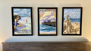 Three framed artworks depicting Jacksonville Beach, Florida, on a wall above a bed.
