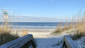 A sandy beach path leading to the ocean, flanked by wooden railings and tall grasses.