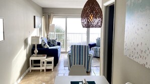 A dining area with a white table, chairs, and a hanging light fixture. There is a blue sofa and striped chairs in the background.