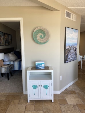 Un salon avec une console blanche, un tableau encadré représentant une plage et une décoration murale.