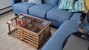 A room with a blue sofa, a wooden coffee table with a glass top, and a laptop on a tray.