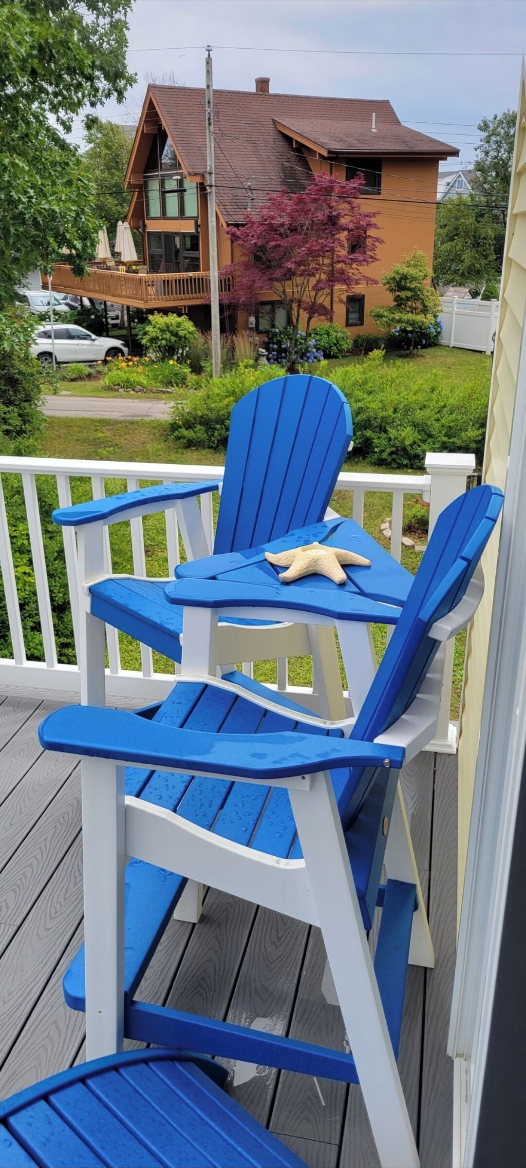 A wooden deck with blue Adirondack chairs and a starfish decoration.