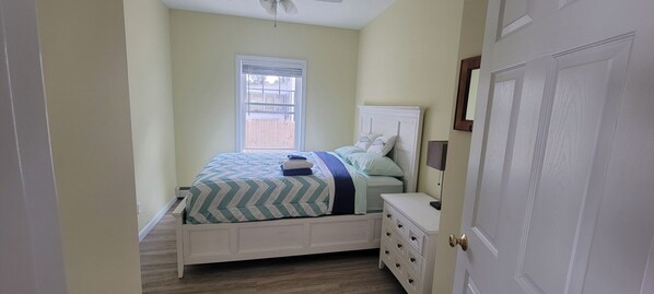 A bedroom with a bed, a nightstand, a dresser, a window, and a door.