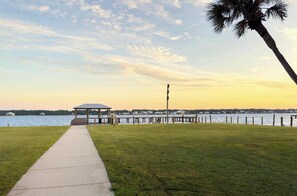 A waterfront walkway leading to a gazebo with a view of the water and distant houses.
