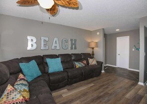 A living room with a sectional sofa, a wall-mounted lamp, and a 'BEACH' sign.