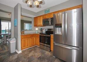 A modern kitchen with wooden cabinets, stainless steel appliances, and a 'Eat' sign on the wall.