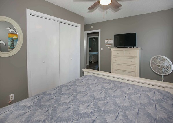 A bedroom with a bed, a dresser, a television, a fan, and a closet.