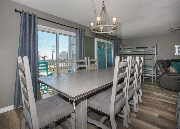 A dining area with a large table and chairs, a chandelier, and a view of the outdoors.