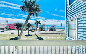 A beachfront property with a balcony overlooking the ocean, a palm tree, and a row of colorful buildings in the background.