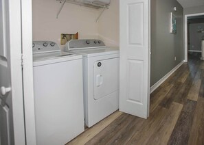 A laundry room with two white washers and dryers, wooden flooring, and a white door.