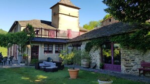 A stone building with a tower, a covered patio with outdoor furniture, and a stone wall with a bench. - Les Copains à Bord - Gîte D'étape (Cans et Cévennes)