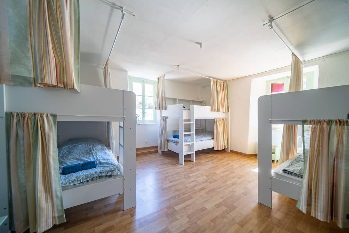 Une chambre avec des lits superposés, un plancher en bois et une fenêtre avec des rideaux.