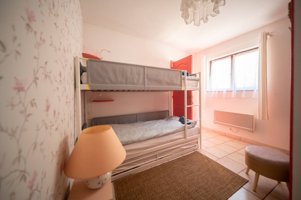 Une chambre avec un lit superposé, une petite tabouret et une fenêtre.