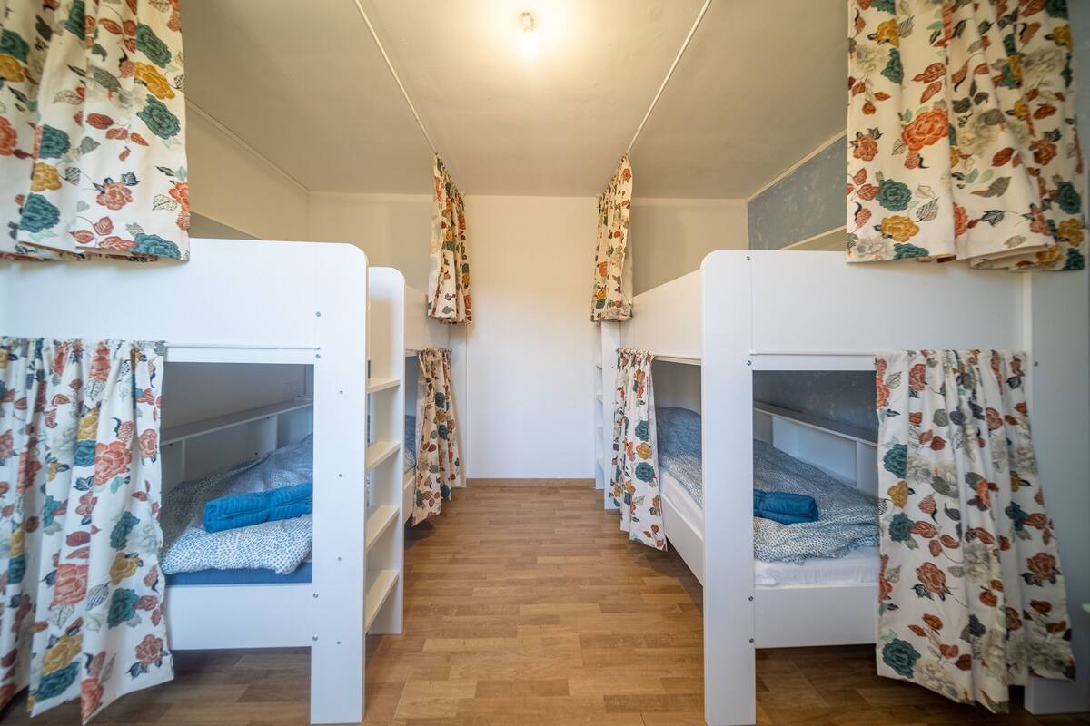 Une chambre de dortoir avec des lits superposés, des rideaux à motifs floraux et un plancher en bois.