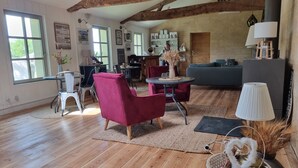 Amplia sala de estar con pisos de madera, un sillón rojo, un sofá gris y una zona de comedor con mesa y sillas.