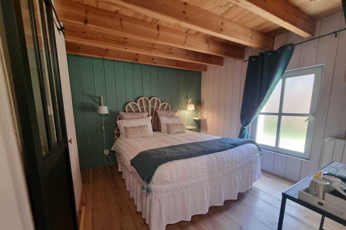 A bedroom with a wooden ceiling, a bed with white bedding, a green wall, and a window with curtains.