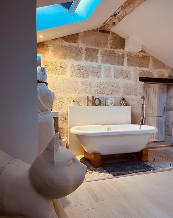 A bathroom with a freestanding bathtub, a stone wall, and a skylight. - Lariviere (Asques)
