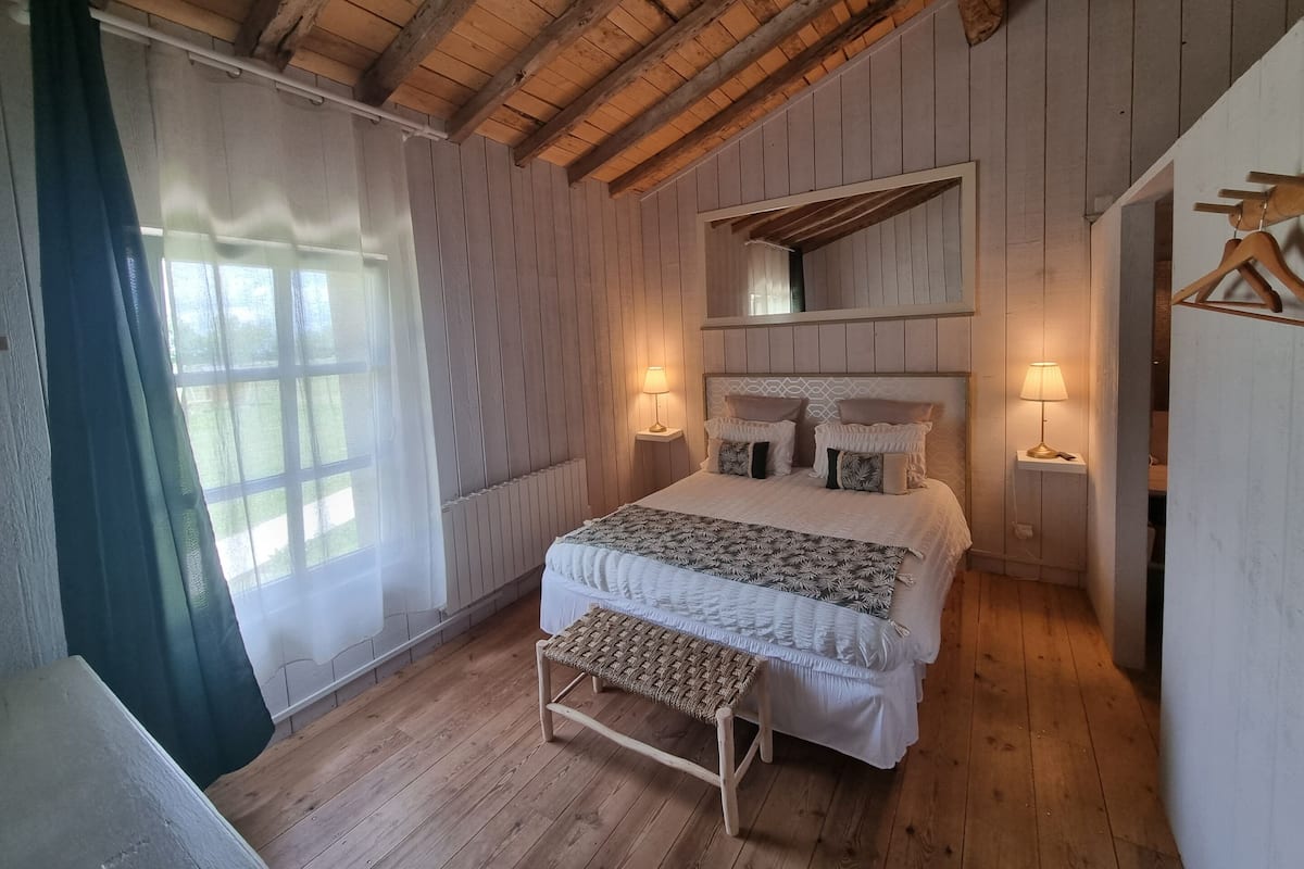 A wooden-paneled bedroom with a bed, two bedside lamps, a bench, and a window with curtains.