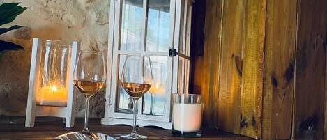 A room with a stone wall, a wooden door, a white cabinet, and a table with two glasses of wine and a candle.