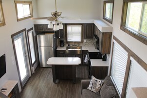 Cocina compacta con refrigerador, estufa y pileta, ventilador de techo y ventana con persianas.